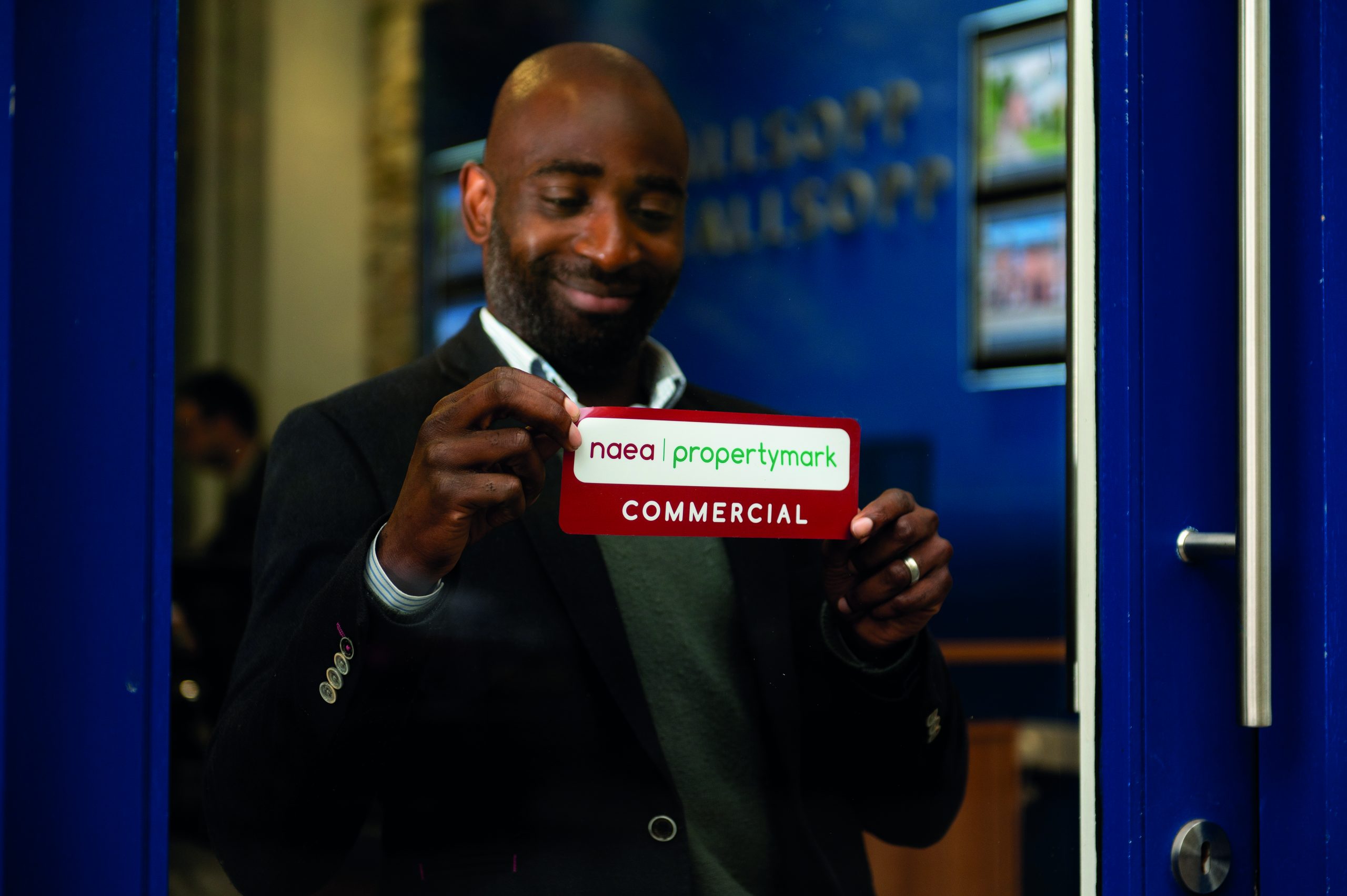 An estate agent putting a Properymark sticker in the window and smiling