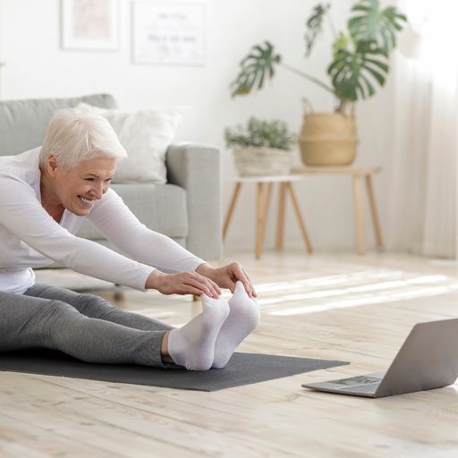 Elderly lady doing stretches and smiling whilst looking at a laptop