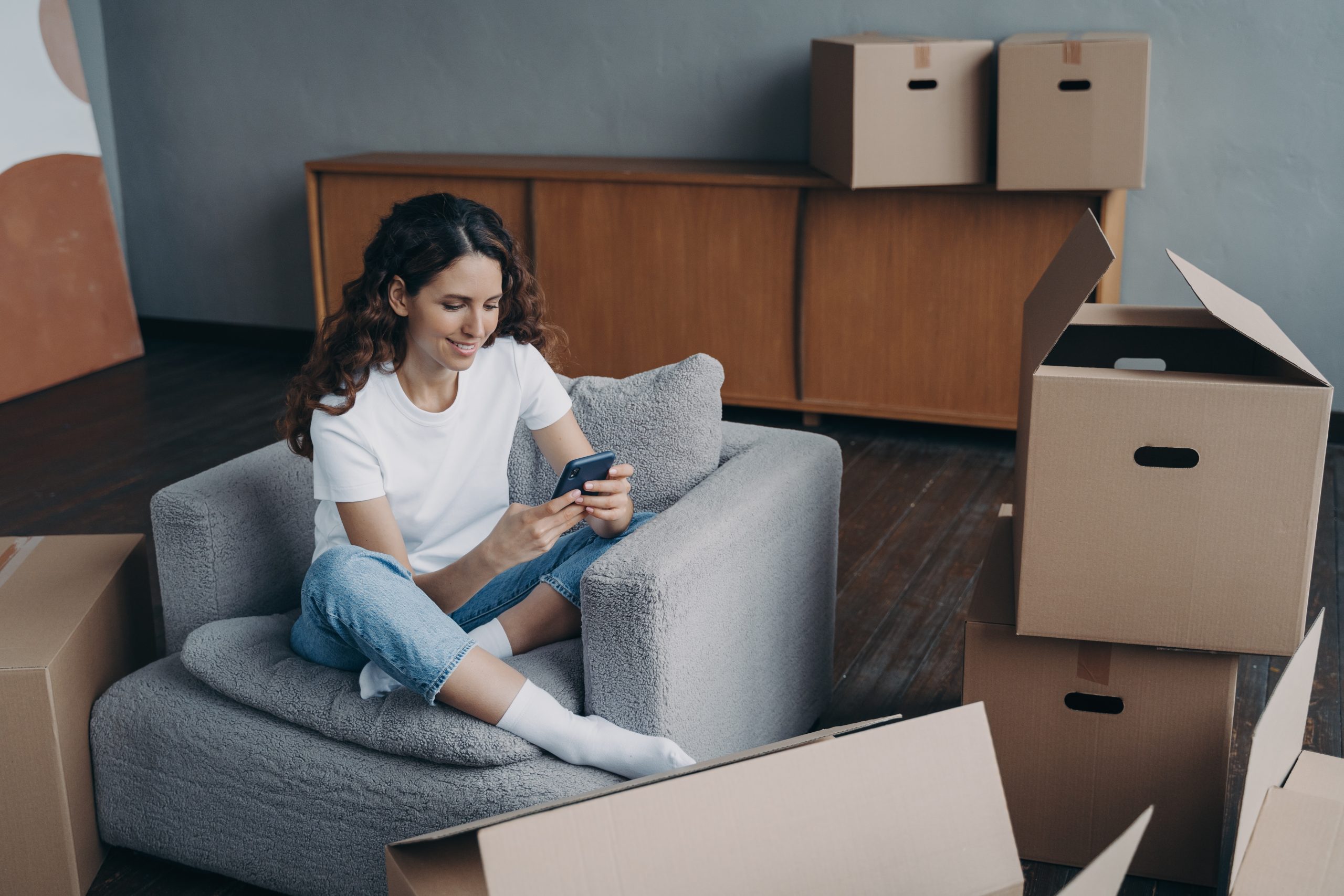 Woman sitting in a chair and smiling at her phone, having just moved into a new house